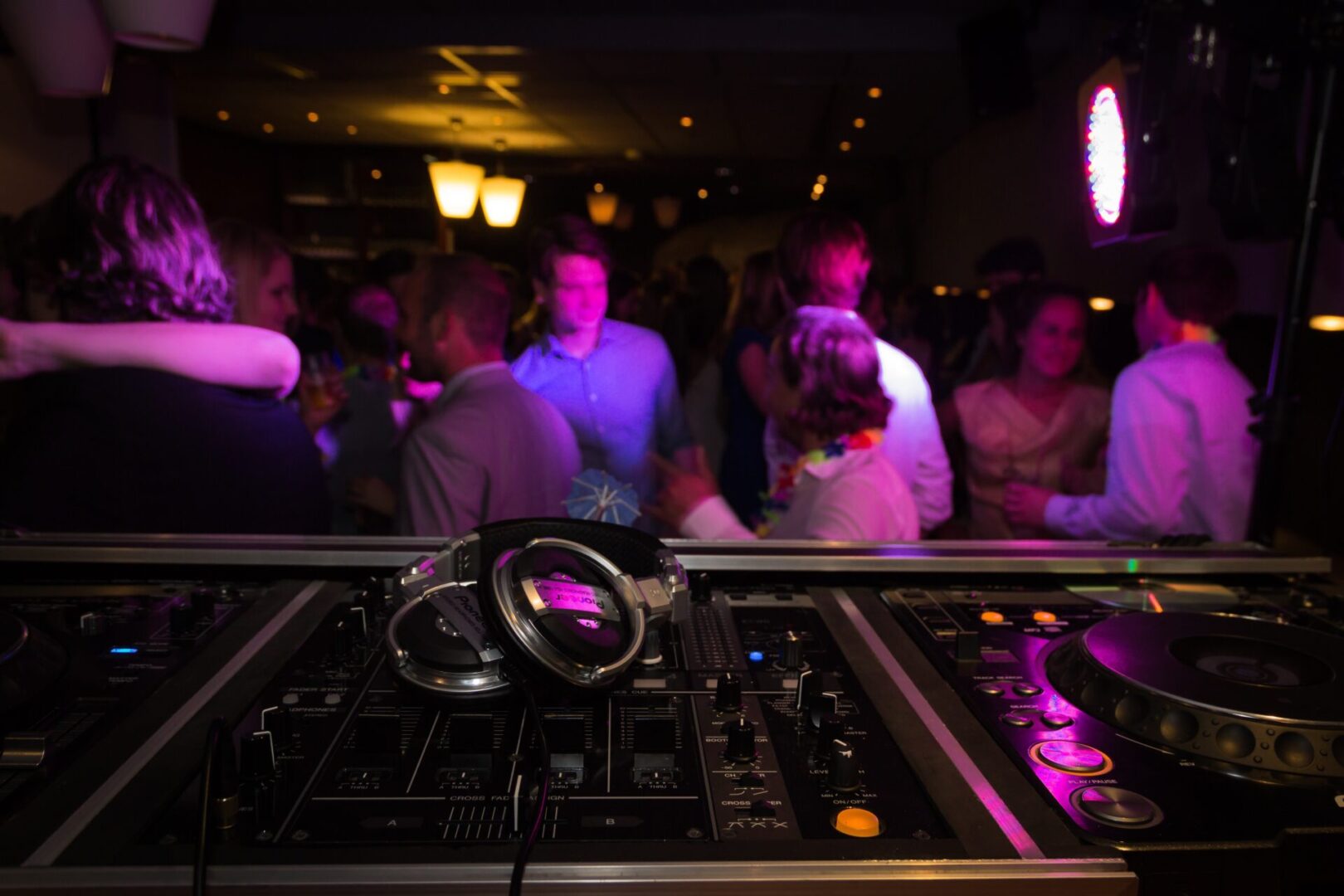 A dj 's table with headphones on it and people watching.